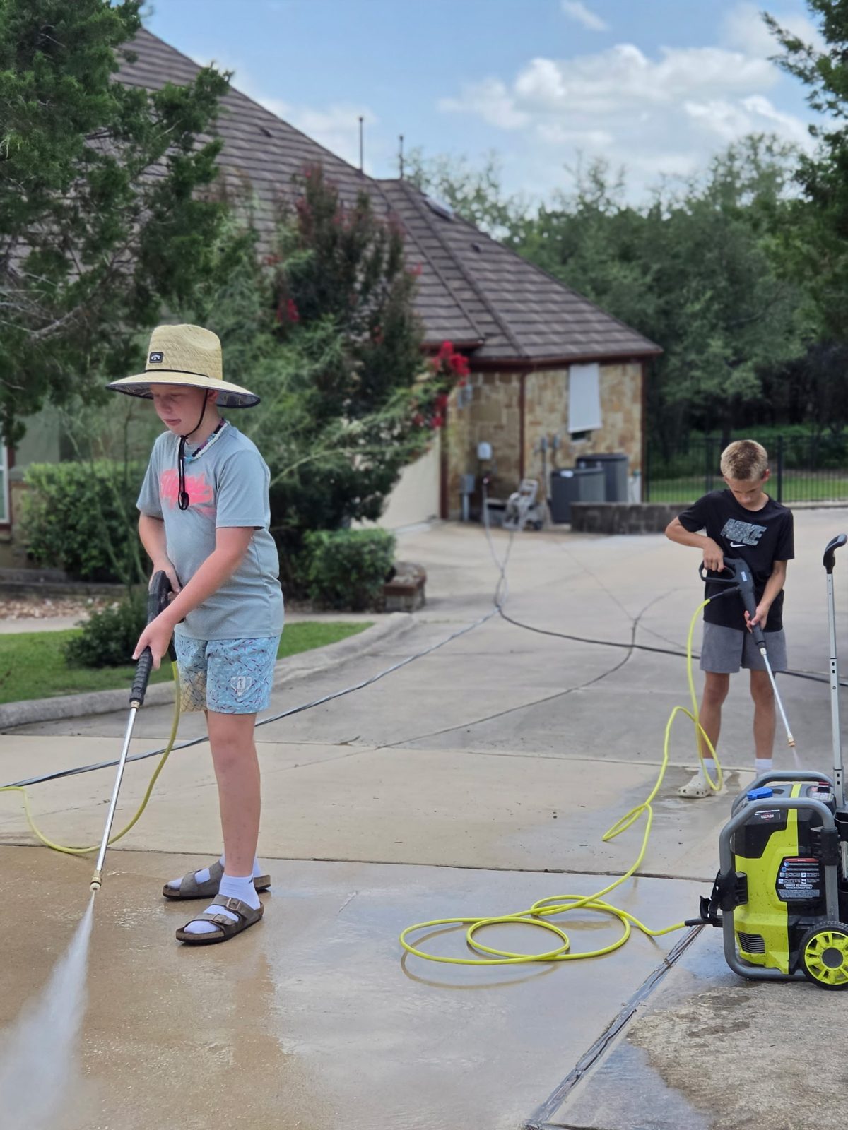 Two D1 crew members power washing a concrete driveway together